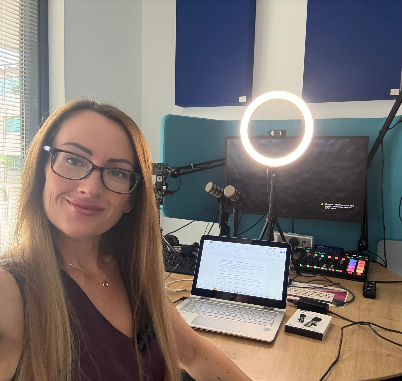 Alexis Drake preparing content in a recording room with a laptop, ring light and microphones.